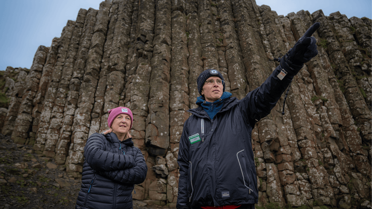 Dr Cliff Henry and Dr Kirstin Lemon stand at the Giant's Causeway, discussing next steps for the Causeway Coin Removal Project beside the iconic basalt columns